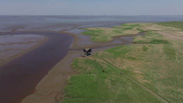 Aerial view of birdwatcher's hut, wetlands, and pathway in serene Wadden Sea, Kiekkaaste, Groningen, Netherlands.