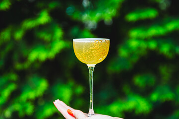 Close-up of a hand holding a glass of yellow cocktail against a blurred green background