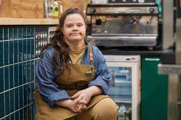 Portrait of independent adult woman with Down syndrome working in cafe and looking at camera with...