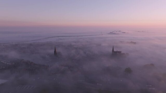 Aerial view of foggy sunrise over church spires in city, Harlingen, Friesland, Netherlands.