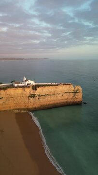 Aerial view of cliff, ocean, chapel, beach, and sky at Ermida de Nossa Senhora da Rocha, Porches, Algarve, Portugal.