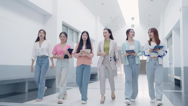 A group of women are walking down a hallway, each holding a tablet. Scene is casual and relaxed, as the women are not wearing formal attire and are simply walking and using their tablets