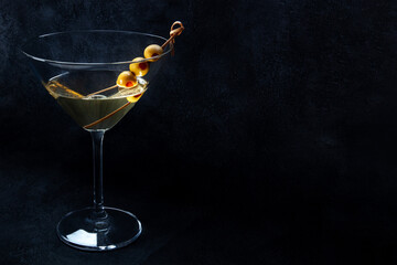 Martini. A glass of dirty martini cocktail with vermouth and olives, on a black background with...
