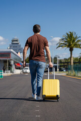 Man arriving at the airport with his yellow suitcase. Young traveling for work or taking a plane to go to university. Man walking through the airport terminal to start his vacation. Man returning home