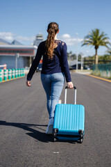 Woman leaving the airport with her blue suitcase. Travel for work or to go to university.  She walks through the airport terminal to start her vacation. Woman returns home.