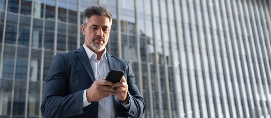Banner with copy space mature hispanic senior business man using smartphone cellphone at office building. Focused serious latin middle age entrepreneur businessman holding mobile cell phone for work