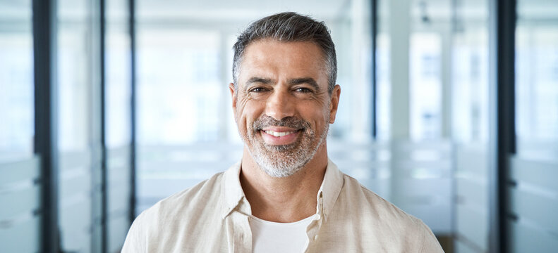 Banner Headshot Close Up Portrait Of Indian Or Latin Confident Mature Middle Age Leader, Ceo Male Businessman On Office Background. Handsome Hispanic Senior Business Man Smiling At Camera, Copy Space