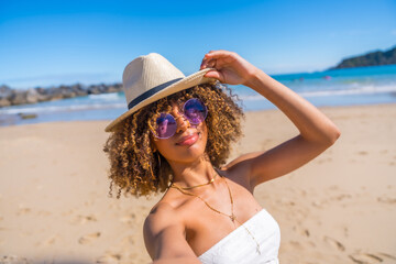 Latin woman holding a sun hat taking selfie a beach