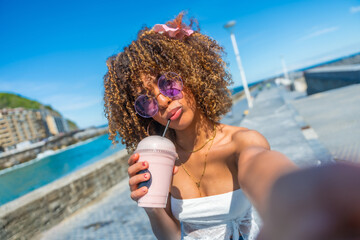 Cool latin woman drinking milkshake taking a selfie on the promenade