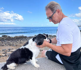 Mature senior man sitting at the beach cuddling his Cavalier King Charles dog. Best friend and love...