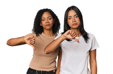 Young Latin friends in studio showing a dislike gesture, thumbs down. Disagreement concept.