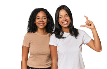 Young Latin friends in studio holding something little with forefingers, smiling and confident.
