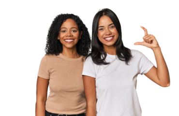 Young Latin friends in studio holding something little with forefingers, smiling and confident.