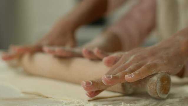 Unrecognizable African American ethnic family close up hands of woman mother female mom teach little child kid daughter girl together cooking dough rolling pin kneading at home kitchen cook baking
