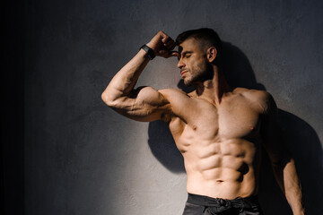 Muscular model sports young man on dark background. Fashion portrait of strong brutal guy. Male flexing his muscles.