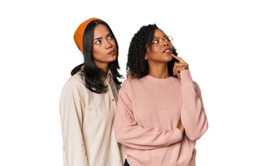 Young Latin friends together in studio looking sideways with doubtful and skeptical expression.