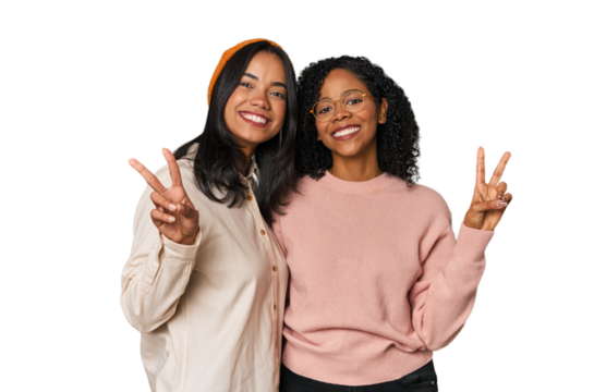 Young Latin friends together in studio showing victory sign and smiling broadly.