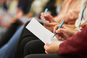 Audience writing in document at conference in auditorium