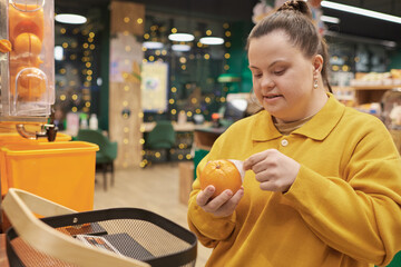 Portrait of cheerful young woman with Down syndrome buying fresh oranges in fruit section of...