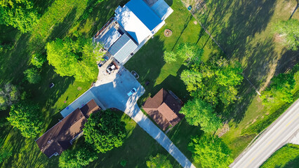Direct aerial view farm houses with long driveway, large storage sheds, acreage lots, lush greenery...