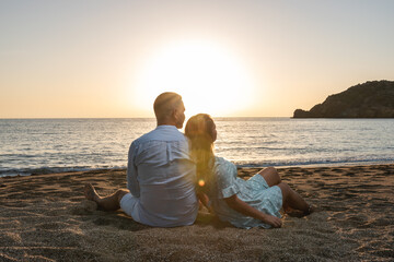 Fototapeta premium Happy couple in love, is seating on the beach during sunset or sunrise. Summer vacations.