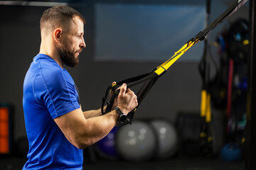 Serious man, strong trainer, athlete doing functional training, holding TRX equipment