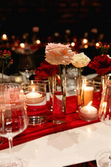 Candlelight date in restaurant. Glasses with wine, bouquet flowers. Romantic dinner setup at night. Table setting for couple, Valentine's Day evening, burning candles for surprise marriage proposal.