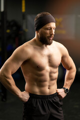 Attractive, bearded man, athlete with naked pumped up torso training in gym, standing looking away
