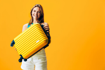 Excited woman ready for adventure, smiling with a bright yellow suitcase on vibrant orange background