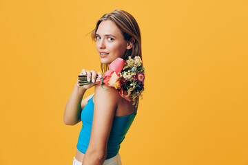 Gorgeous woman smiling and holding colorful bouquet of flowers in front of vibrant yellow wall