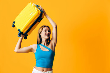 Vibrant woman in blue top joyfully raises suitcase aloft against bright orange background