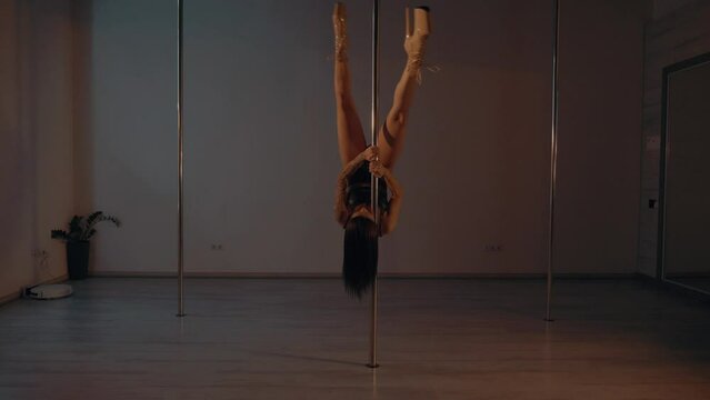 Woman in leather underwear gracefully pole dancing in a dimly lit room. Elegant female in a bikini performer doing a seductive dance on a pole. Lady showing her strength and flexibility on the pole. S
