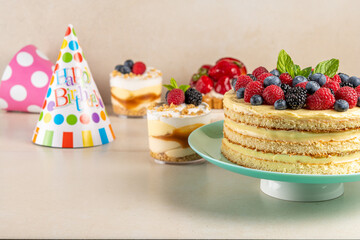 Homemade cake with fresh berries and birthday hat on bright background.