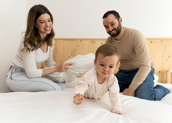 Family of three playing on a bed: man, woman, and baby smiling in a delightful scene