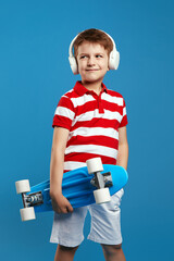 Vertical photo of handsome kid wearing red striped polo shirt, holding skateboard and listening...
