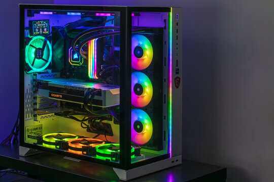 Adelaide, Australia - December 24, 2023: Close-up view of modern gaming PC in glass case with RGB glowing LED lights, CPU water cooling and NVidia GeForce RTX graphics card while working in dark room