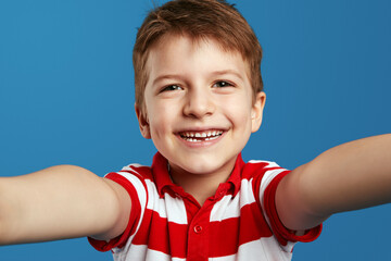 Funny child boy in red striped polo shirt looking at camera in amazement and taking selfie against...