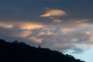 Obraz premium Landscape of thick clouds, orange light hitting the blue sky, silhouettes of trees, forests, and mountains. Area for text in the middle of the image