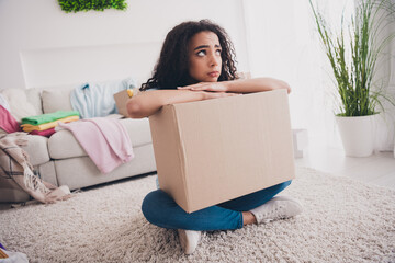 Full size photo of nice young girl sit floor think hold clothes things box apartment indoors
