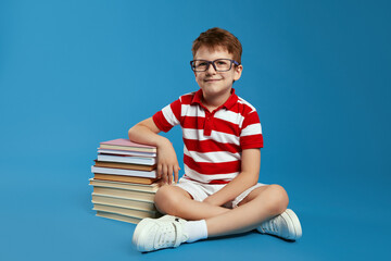 Little genius kid in red striped shirt and eyeglasses smiling and looking at camera while sitting...