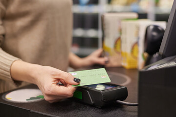 Close up of female hand holding credit card paying via NFC in grocery store, copy space
