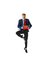 Focused on work young man in formal attire stands in yoga tree pose and holds folder against white...