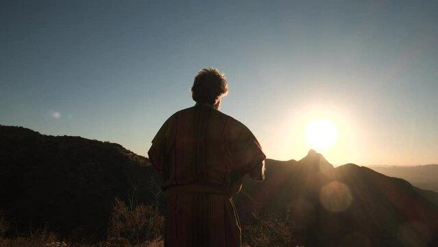 A Bible prophet raises his arms on a mountain at sunset