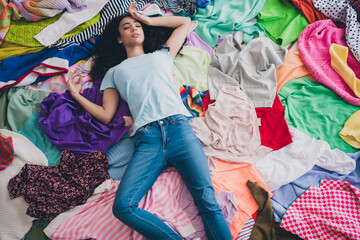 High angle view photo of young girl laying pile stack clutter clothes apartment indoors