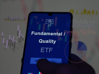 An investor analyzing the fundamental / quality etf fund on a screen. A phone shows the prices of...