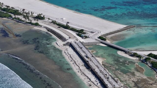 Aerial view of coastal road construction with palm trees and turquoise water, Maradhoo, Addu Atoll, Maldives.