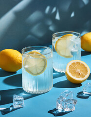 Refreshing summer drinks setup with lemon slices and ice on blue background 