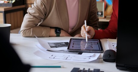 Architects discussing layout on digital tablet, focusing on floor plan details. Meeting modern technology integration in architectural design. Collaborative workflow in contemporary office setting.