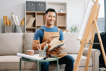 Asian male painter do artwork in art workshop, painting supplies, oil pastels, two canvas easel, creative space with paintbrush
