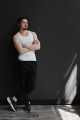 A confident man in casual clothing leans against a dark wall, exuding a relaxed and contemplative vibe.